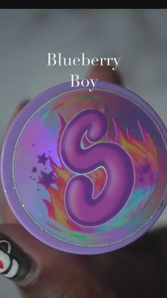 Blueberry Boy pomade in a purple container with vibrant flames and shimmering stars design.
